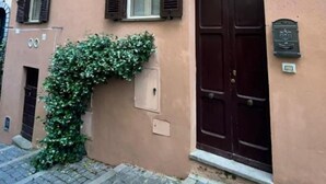 A building with a brown facade, a dark brown arched door, and a window with shutters.