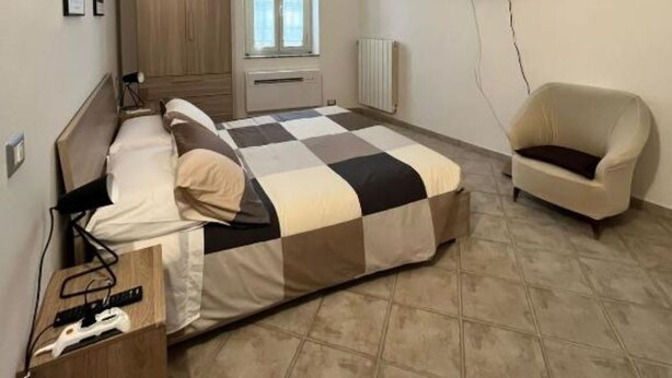 A bedroom with a bed, a chair, a TV, and a window.