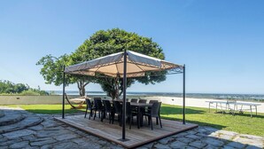 Un patio al aire libre con una mesa y sillas bajo una marquesina, una hamaca y vista al mar.