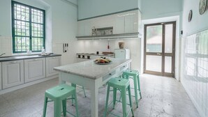 Una cocina con armarios blancos, encimera de mármol y taburetes verdes.