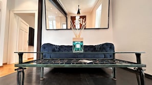 Ein modernes Wohnzimmer mit einem Glastisch, einem dunkelblauen Sofa und einer Pendelleuchte.