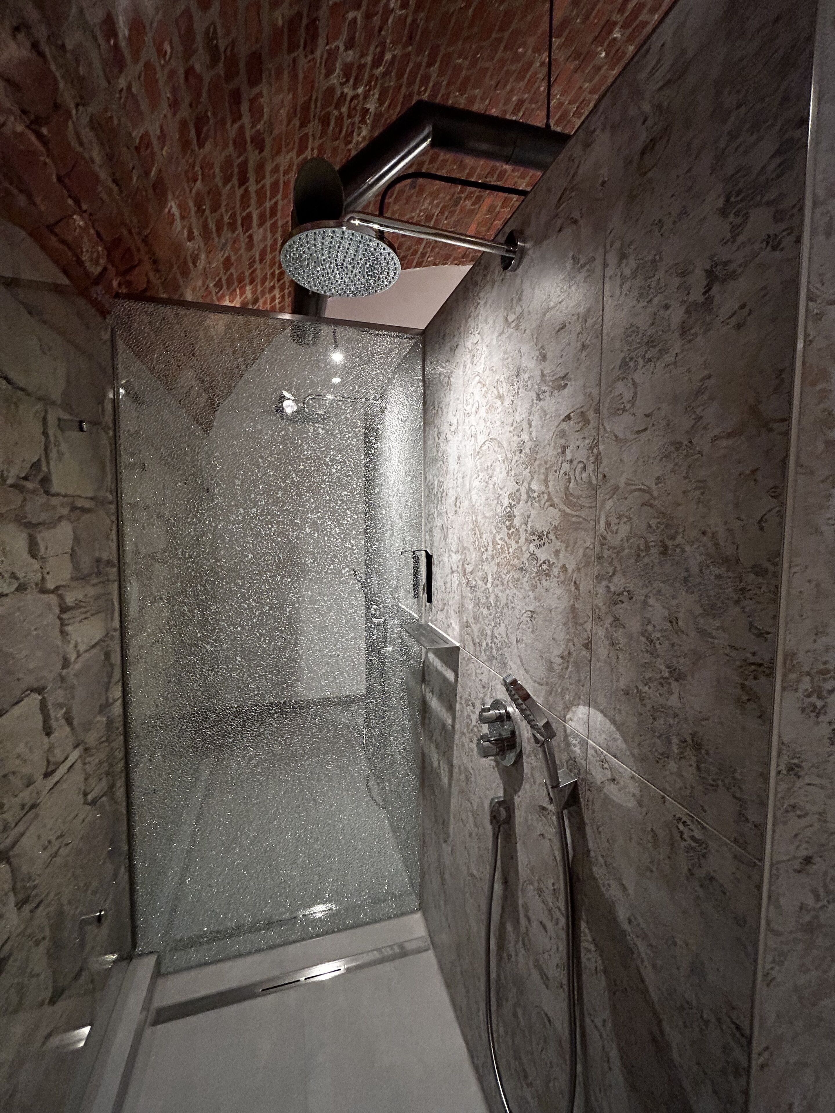 Een douche met een glazen deur, een handdouche en een apart douchemondstuk.