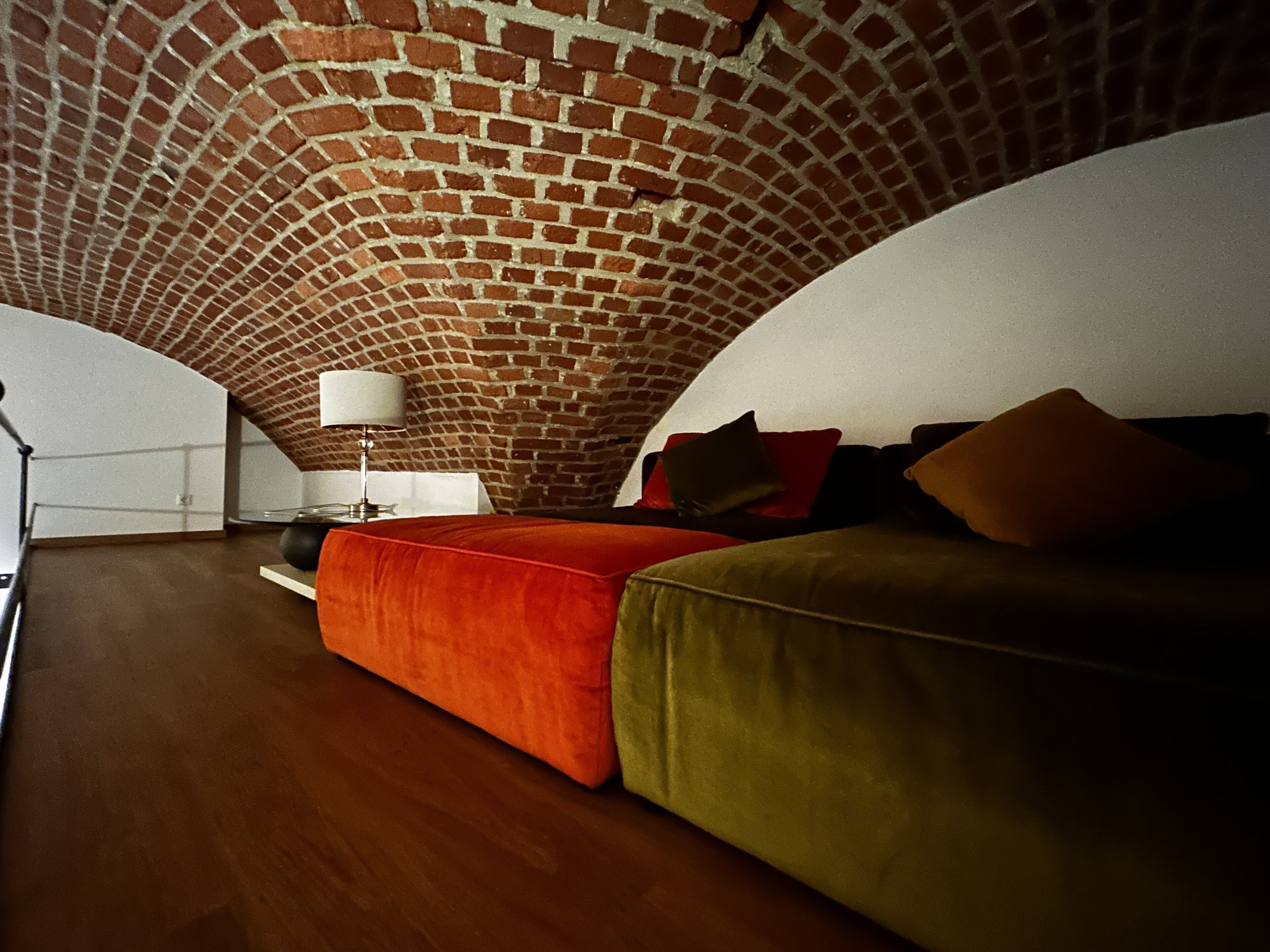 Una camera da letto mansardata accogliente, con soffitto in mattoni, pavimento in legno e letto con biancheria rossa e verde.