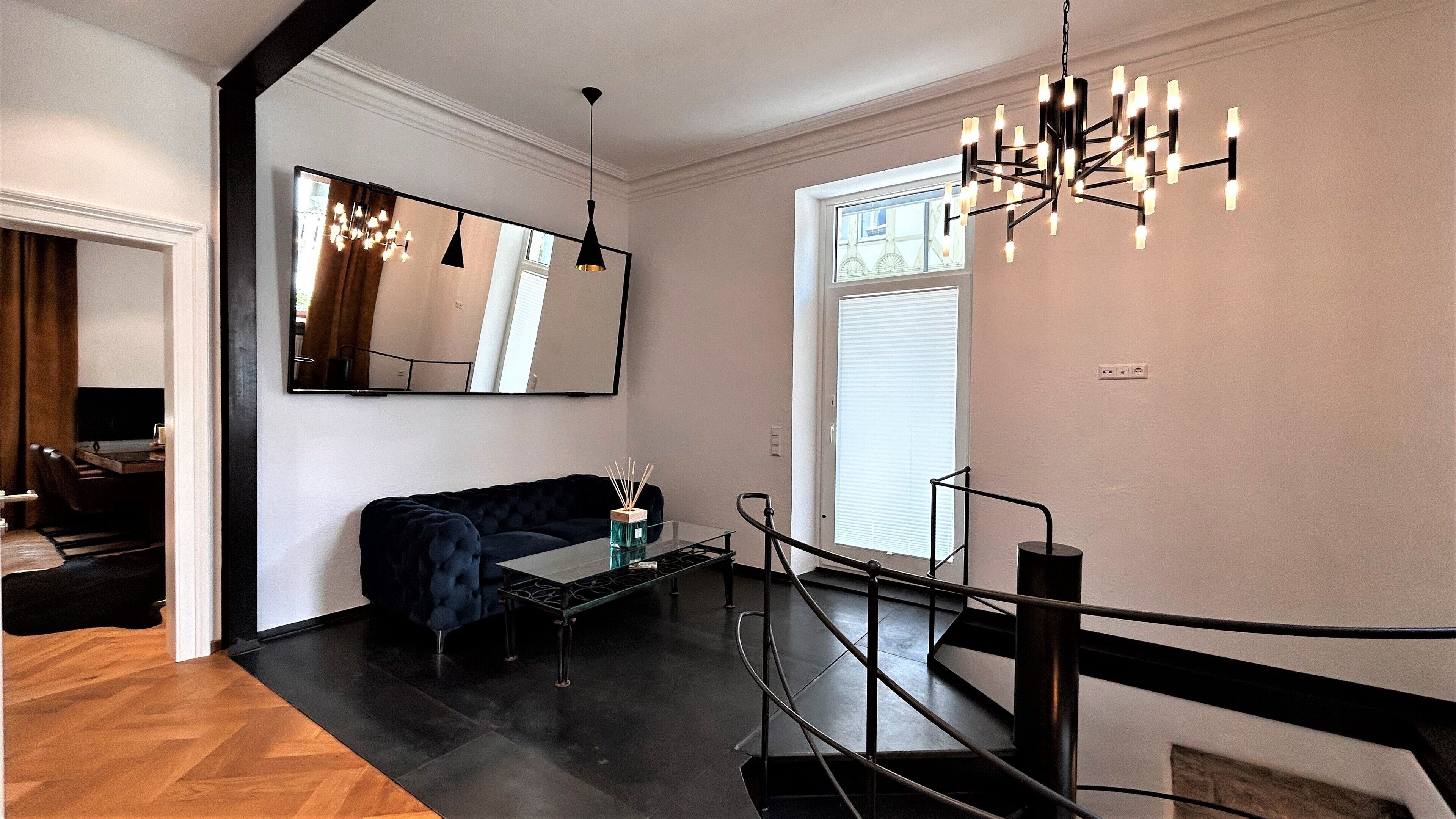 Un salon moderne avec un canapé bleu foncé, une table basse en verre et un lustre noir.
