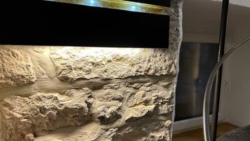 En vägg med en strukturerad stenbeklädnad och ett svart, horisontellt element, eventuellt en hylla eller en panel, samt en metallkonstruktion till höger.