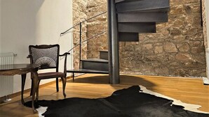 Een modern interieur met een spiltrap, stenen muren, een houten eettafel en een zwart-wit koehuidkleed.
