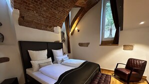 Een slaapkamer met een groot bed, een bankje, een stoel en een raam met uitzicht op groen.