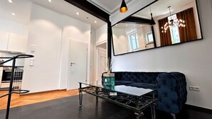 Een moderne woonkamer met een donkerblauwe bank, een glazen salontafel en een grote spiegel aan de muur.