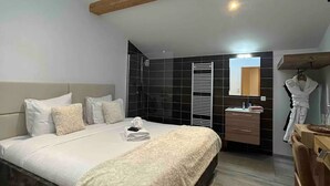 A bedroom with a skylight, a bed with a white duvet, a wooden dresser, and a black tiled wall.