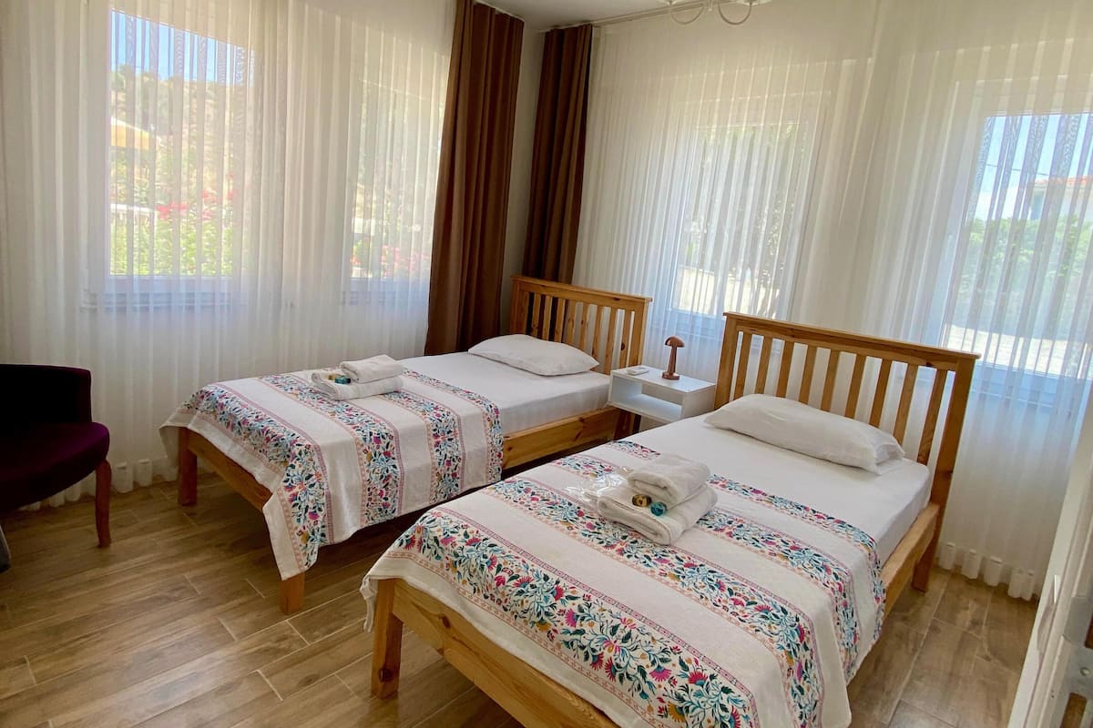Habitación de hotel con dos camas de madera, una silla de madera y una mesita de noche con lámpara.