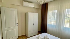 A hotel room with a bed, a wardrobe, an air conditioning unit, and a window with curtains. - Aura Bozcaada (Bozcaada)