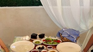 A table set with various dishes, including bread, vegetables, and condiments. - Aura Bozcaada (Bozcaada)