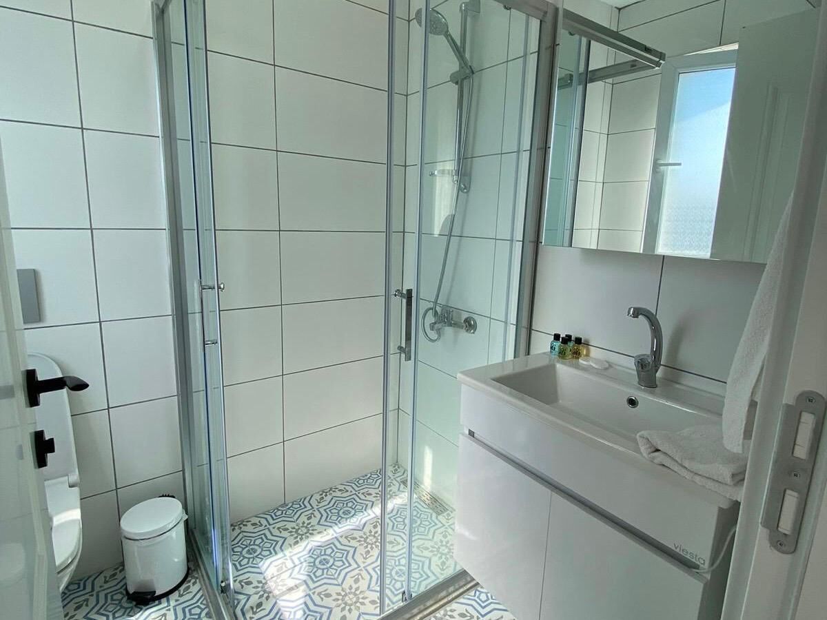 A modern bathroom with a glass-enclosed shower, white tiles, a sink with a mirror, and patterned floor tiles.