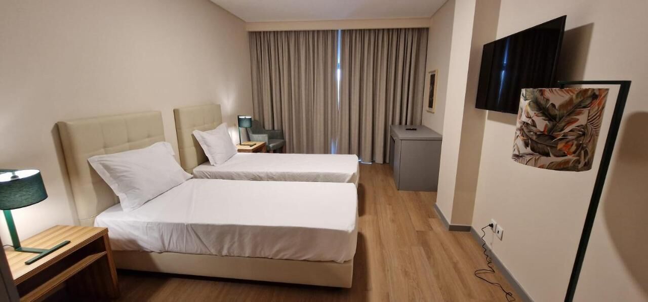 A hotel room with two beds, a desk, a chair, a TV, and a window with curtains.