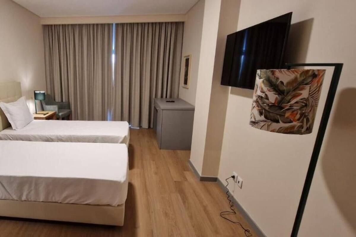 A hotel room with two beds, a desk, a chair, a TV, and a window with curtains.