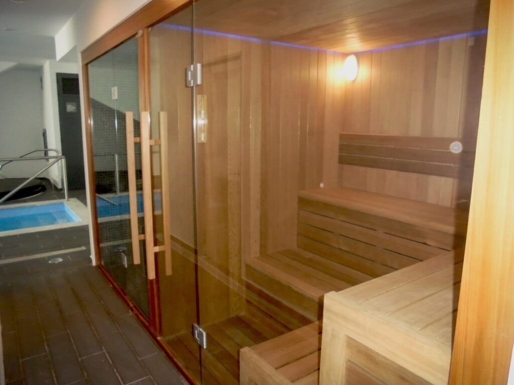 A sauna with wooden benches and a glass door, a small pool area, and a wooden bench outside.