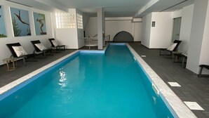 An indoor swimming pool with a tiled floor and a clear blue pool. There are lounge chairs and a staircase leading to a higher level. - Villa Rey Hotel & Spa (Vila de Rei)
