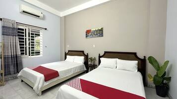 Two single beds with red accents, a large window, and a potted plant.