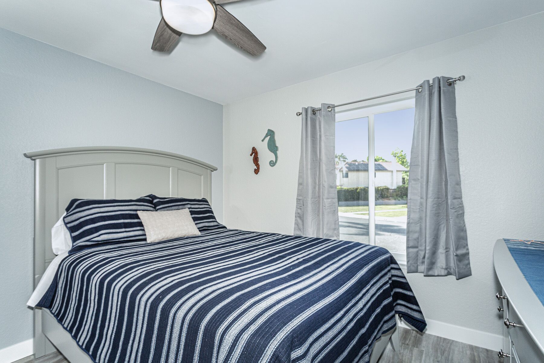 A bedroom with a bed, a ceiling fan, a window with curtains, and a small desk with a chair.