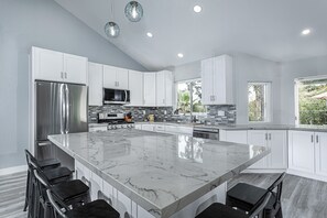 A modern kitchen with a large marble island, stainless steel appliances, and white cabinetry.