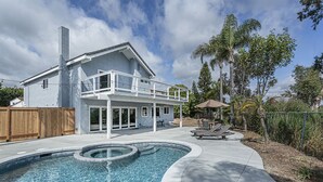 Une maison à deux étages avec une piscine dans le jardin, une terrasse couverte et une clôture en bois.