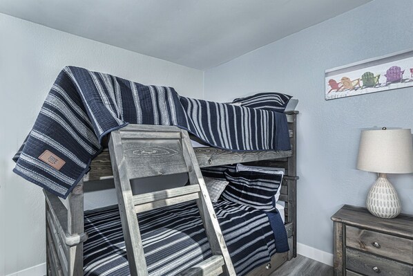 A bunk bed with striped bedding, a wooden ladder, a lamp, and a small dresser.