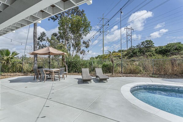 Un área de piscina con zona de estar cubierta, sillas de descanso y una pérgola.