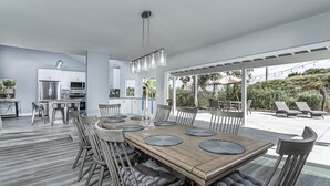 A spacious dining area with a wooden table and chairs, a kitchen in the background, and a patio with lounge chairs and an umbrella. - ~OPEN 9/14-17! Beachy Lagoon Getaway! Pool & Spa, Pets OK, Remodeled!~ (Carlsbad)