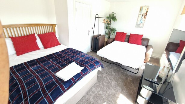 A hotel room with a bed, a sofa, a TV, and a door. - NightRest Homes 6 Bedroom Short & Long Term Smart Tv in each Room, Free Parking  (Oxley Park)