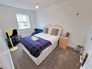 A bedroom with a bed, a bedside table, a lamp, a chair, a desk with a computer, and a window. - NightRest Homes 6 Bedroom Short & Long Term Smart Tv in each Room, Free Parking  (Oxley Park)