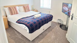 A bedroom with a bed, a nightstand, a lamp, a television, a window with blinds, and a wall-mounted artwork. - NightRest Homes 6 Bedroom Short & Long Term Smart Tv in each Room, Free Parking  (Oxley Park)