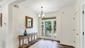 Un couloir avec une console en bois, un miroir et un tapis menant à une porte vitrée donnant sur l’extérieur.