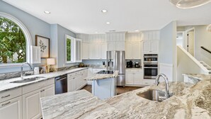 Une cuisine moderne avec des meubles blancs, un grand îlot central doté d’un évier et des appareils électroménagers intégrés.
