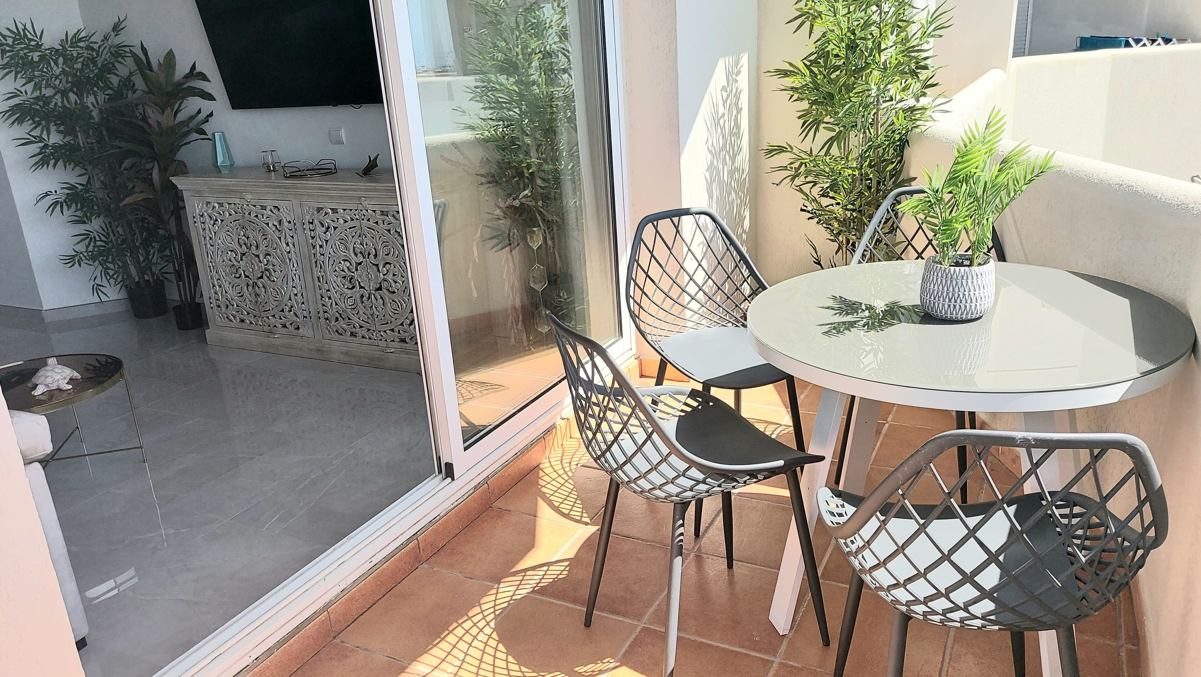 A balcony with a glass door, a round table with chairs, and potted plants.