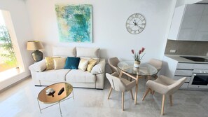 A modern living room with a sofa, chairs, a glass coffee table, a clock, and a kitchen area. - Benal Beach. Beautiful penthouse in first line beach.4 people. 5 swimming pools. (Benalmadena)