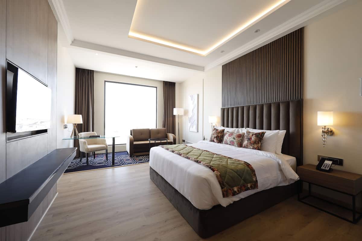 A modern hotel room with a large bed, a desk, a chair, and a TV.