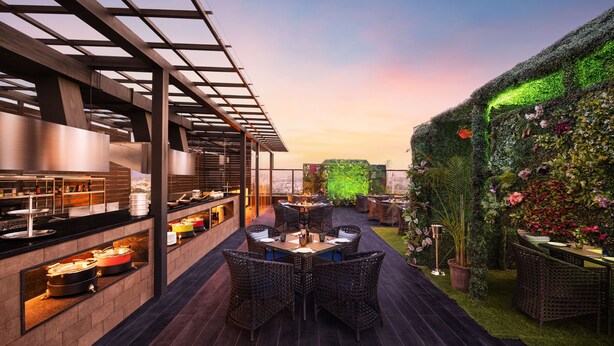 An outdoor dining area with a modern design, featuring a long table with chairs, a pergola structure, and a wall covered in greenery. - Fortune Ranjit Vihar, Amritsar - Member ITC Hotels' Group (Amritsar)