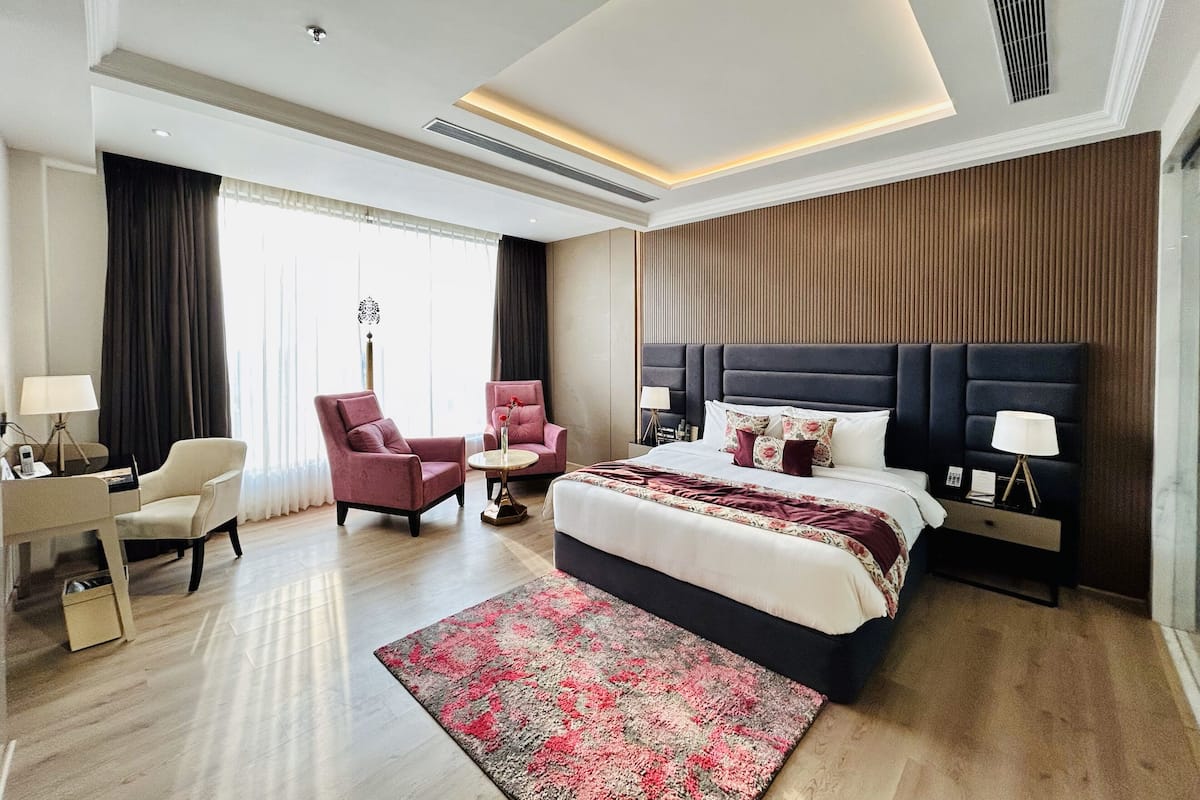 A modern hotel room with a large bed, two armchairs, a small table, and a nightstand with lamps.