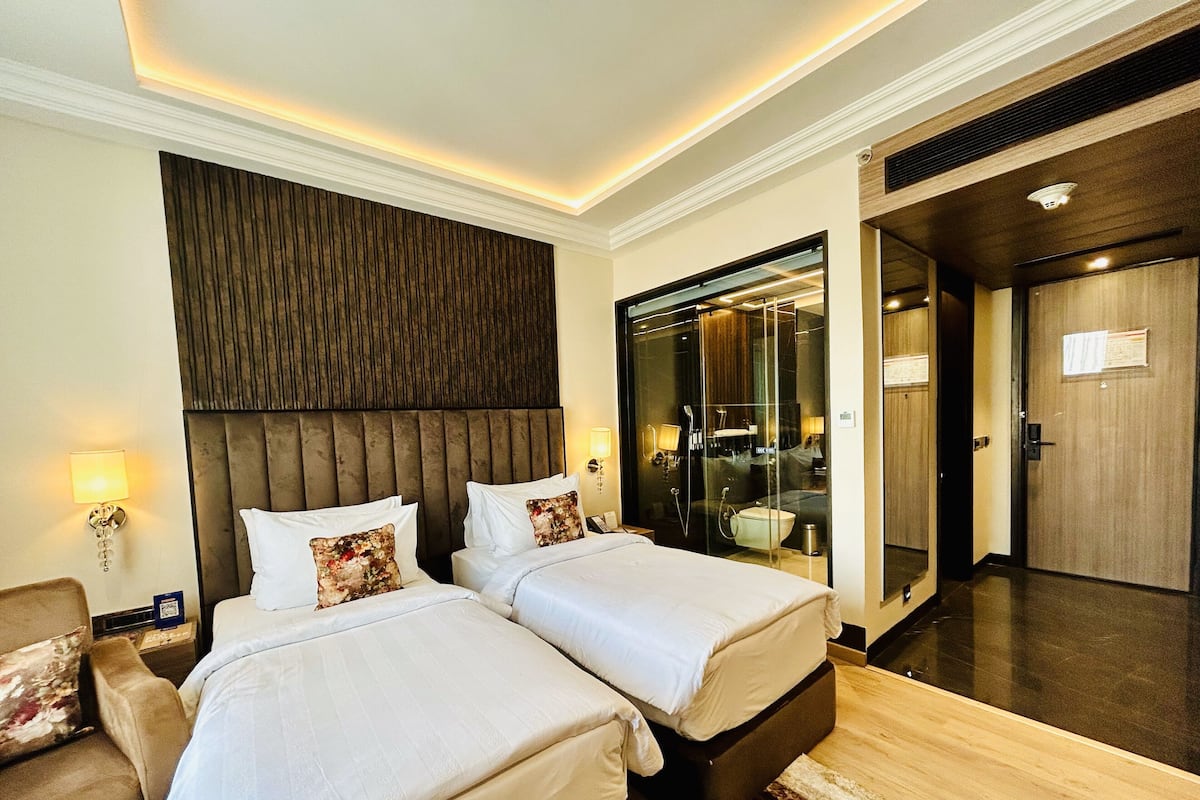 A hotel room with two beds, a large mirror, and a glass-enclosed shower area.