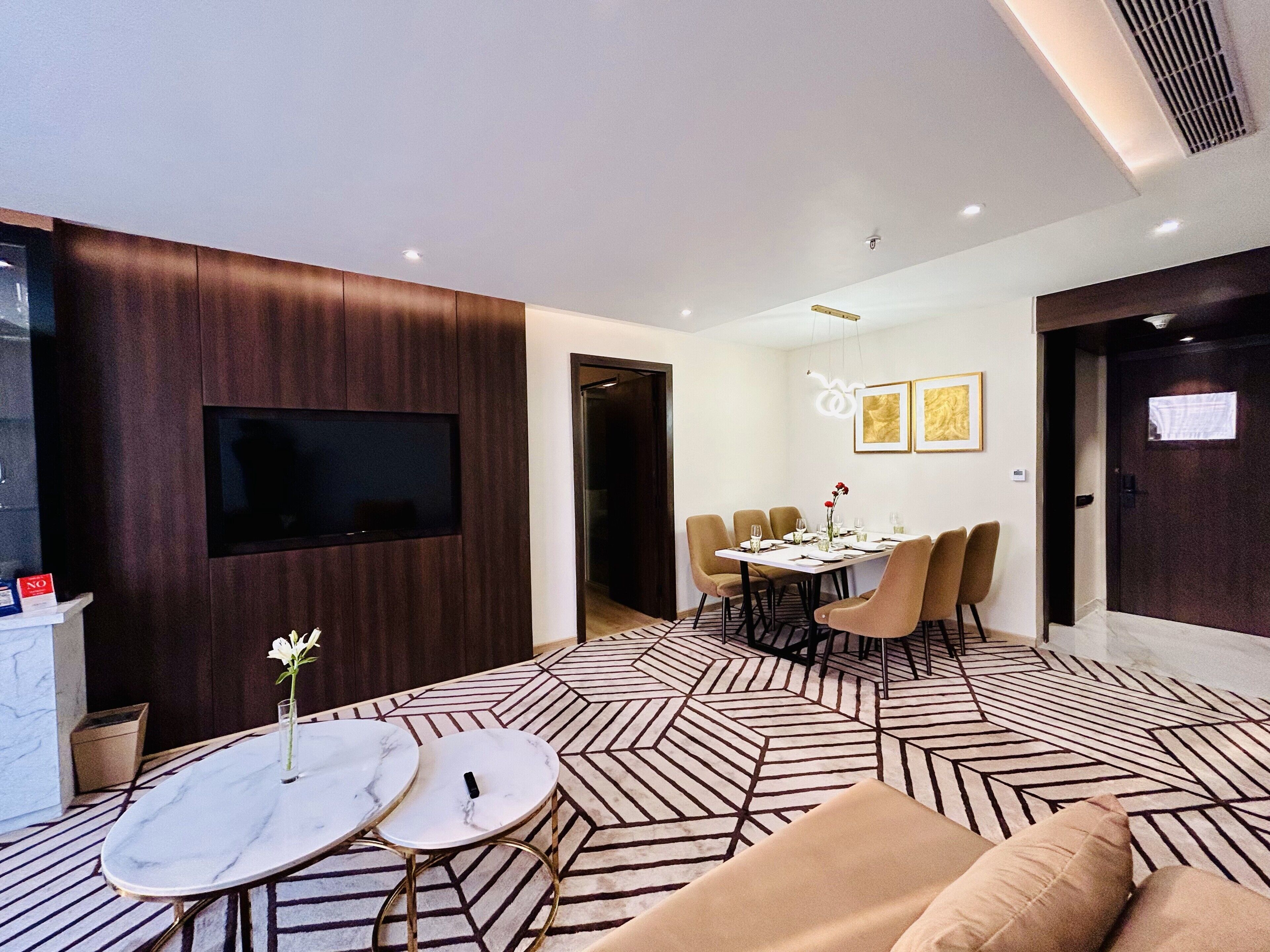 A modern living room with a TV, two marble tables, a sofa, and a dining area with chairs and a table set for four.