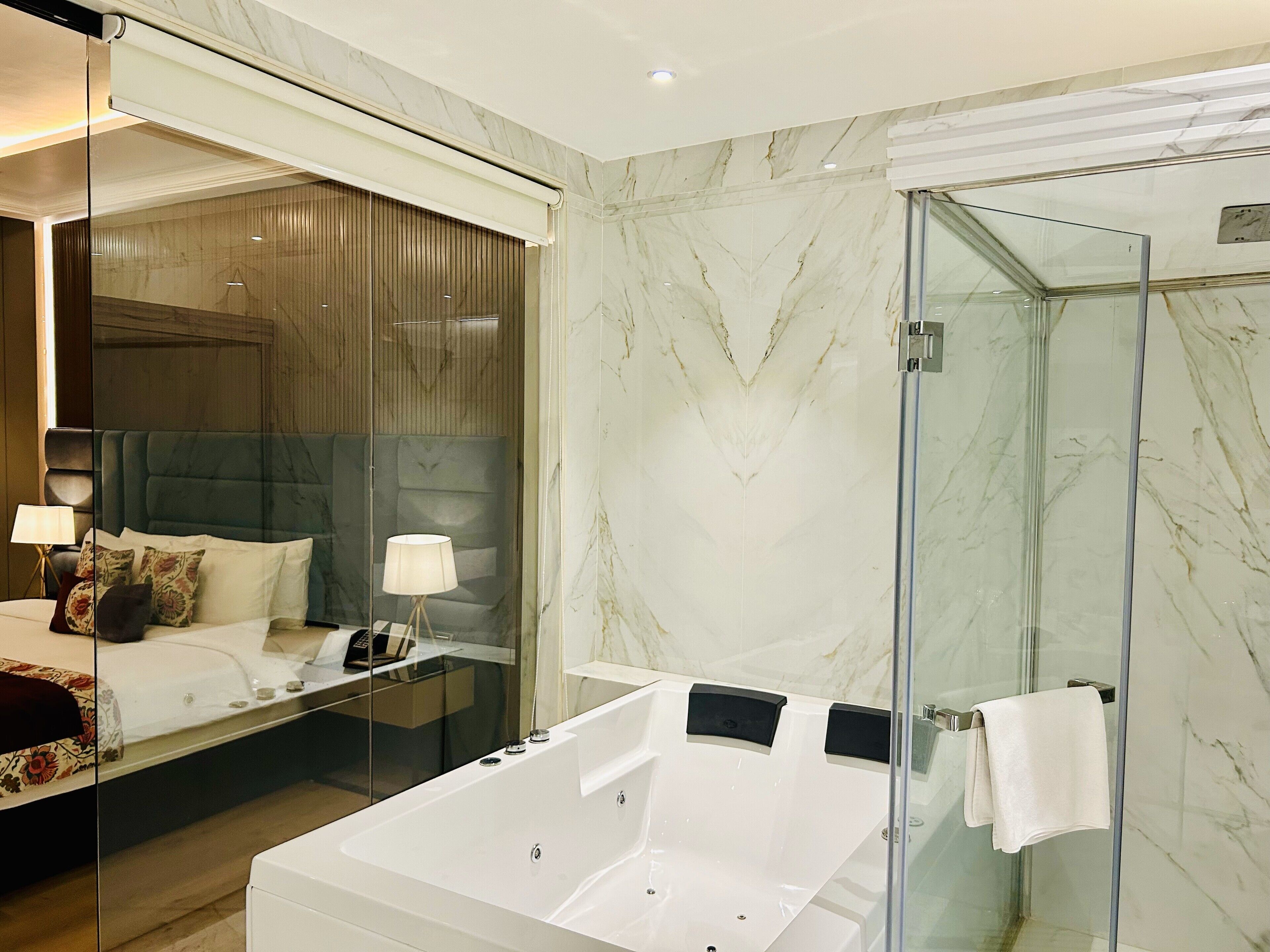 A modern hotel room with a large bed, a glass-enclosed shower, and a separate bathroom with a bathtub.