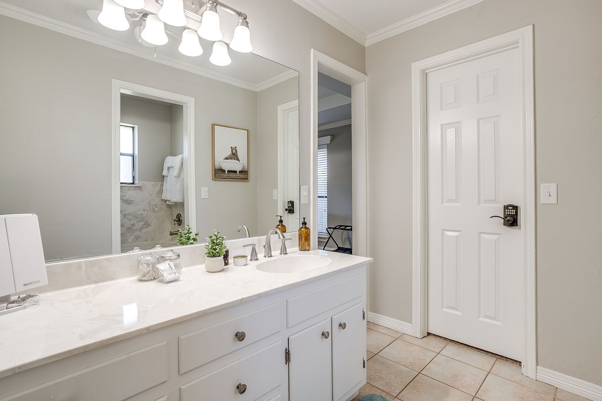 Une salle de bain avec un meuble-lavabo blanc, un grand miroir et une porte donnant sur un placard.