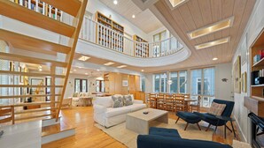 Ein großzügiger Wohnbereich mit einem weißen Sofa, blauen Sesseln, Holzböden und einer Treppe zu einer Erschließungsebene mit Bücherregalen.