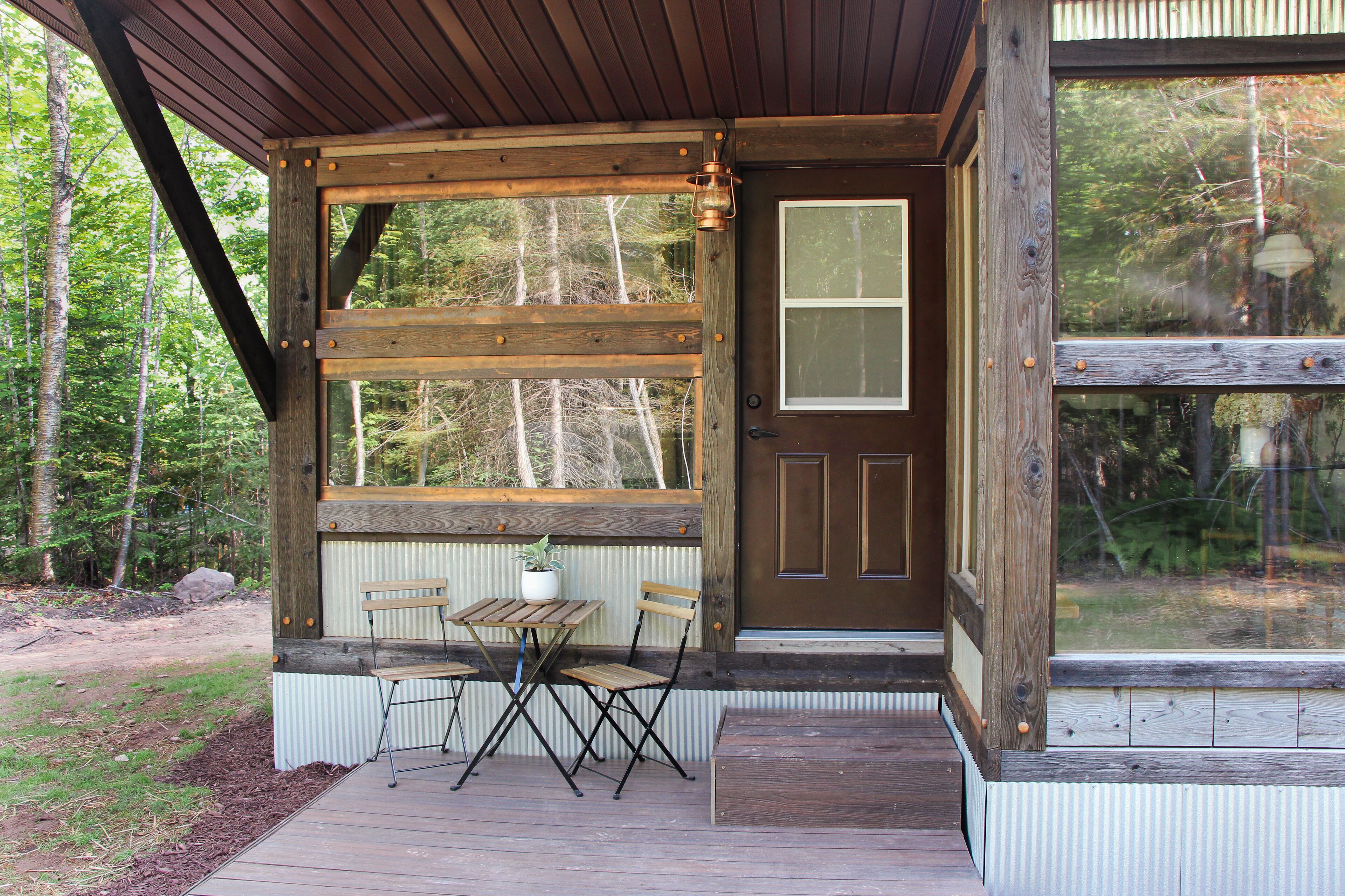 A wooden cabin with a porch, a table, and two chairs.