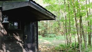 Una cabaña de madera rústica con un porche, rodeada de un bosque denso.