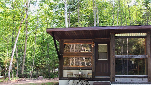 Una cabaña con fachada de madera, ventanas amplias y un pequeño patio con mesa y sillas.