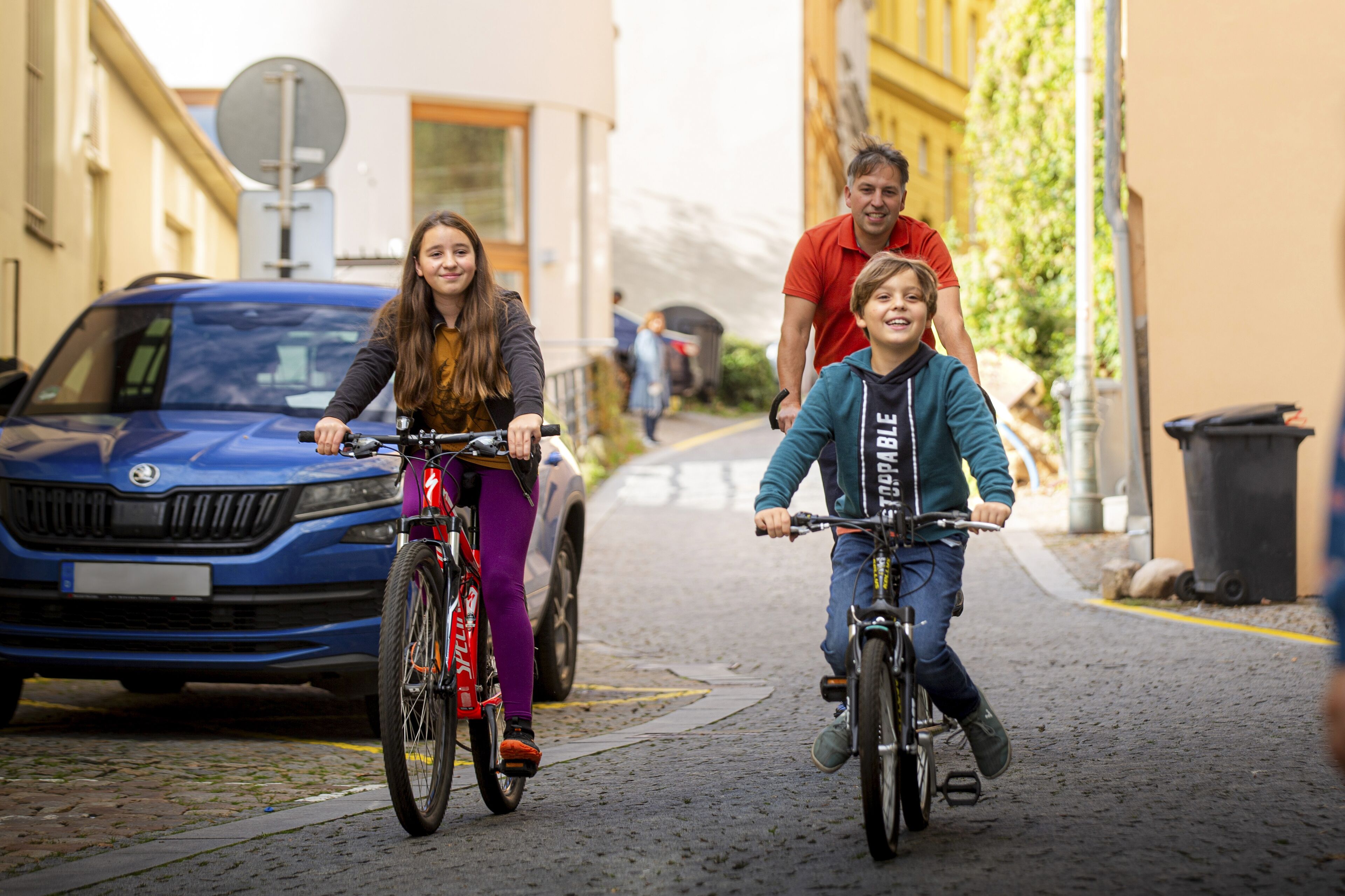 Tre persone che vanno in bicicletta su una strada acciottolata, fiancheggiata da edifici.