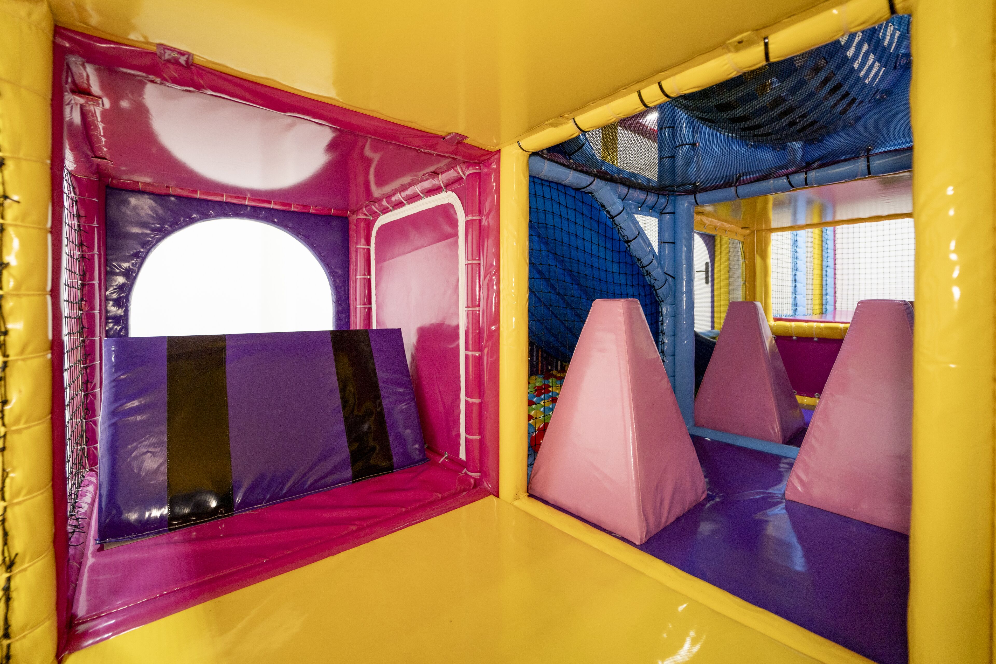 Zona de juegos interior con asientos acolchados y estructuras de juego cubiertas con red.