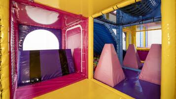 Zona de juegos interior con asientos acolchados y estructuras de juego cubiertas con red.