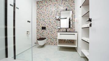 A bathroom with a mosaic tile wall, a glass shower enclosure, a white sink with a mirror, and a toilet.